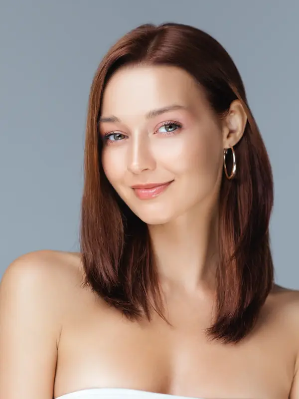 Woman with bare shoulders smiling softly against a grey background