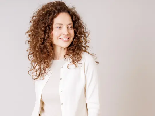 Smiling woman with curly hair in a soft cream cardigan